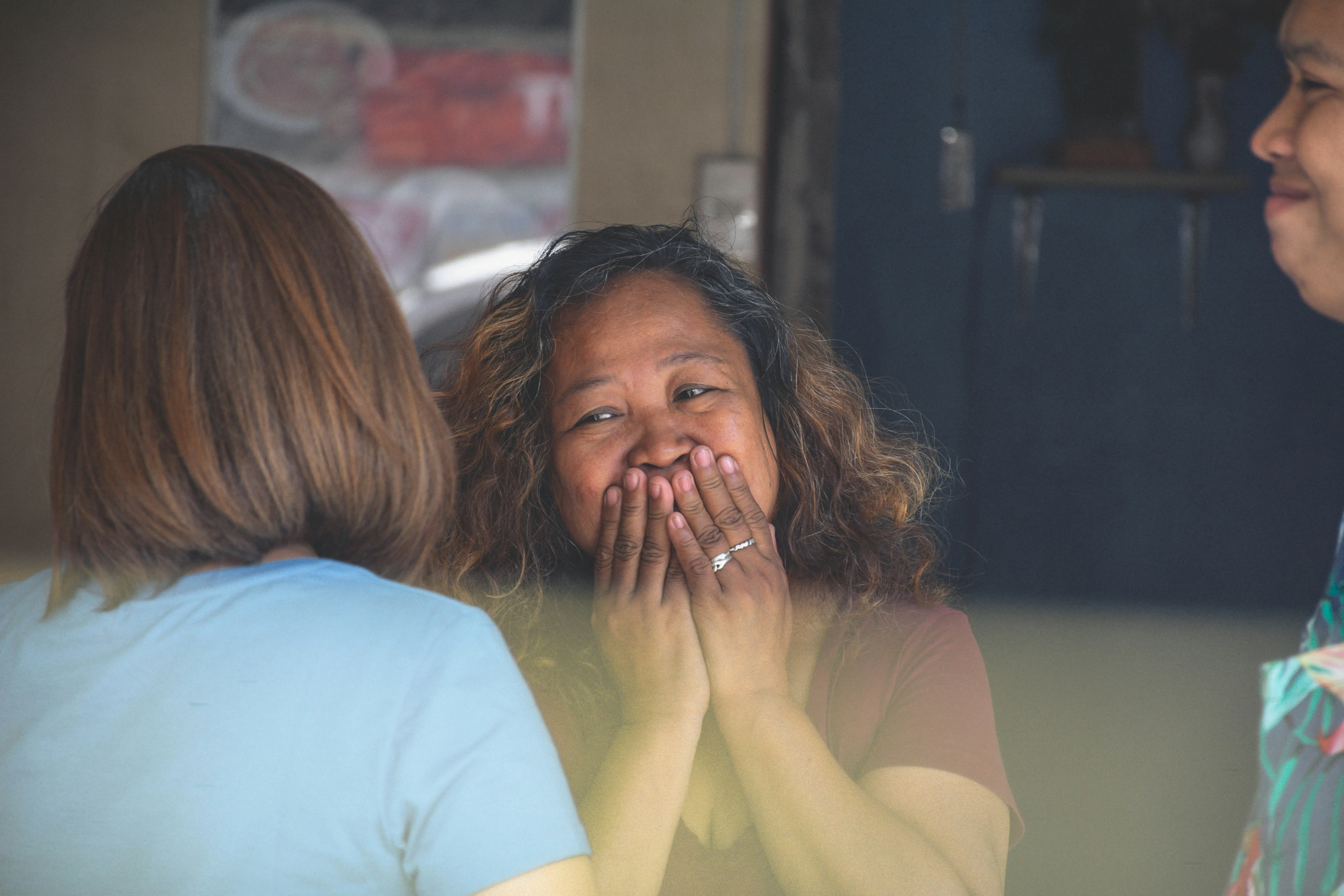 A woman laughing with her hands over her mouth, talking with friends at a table