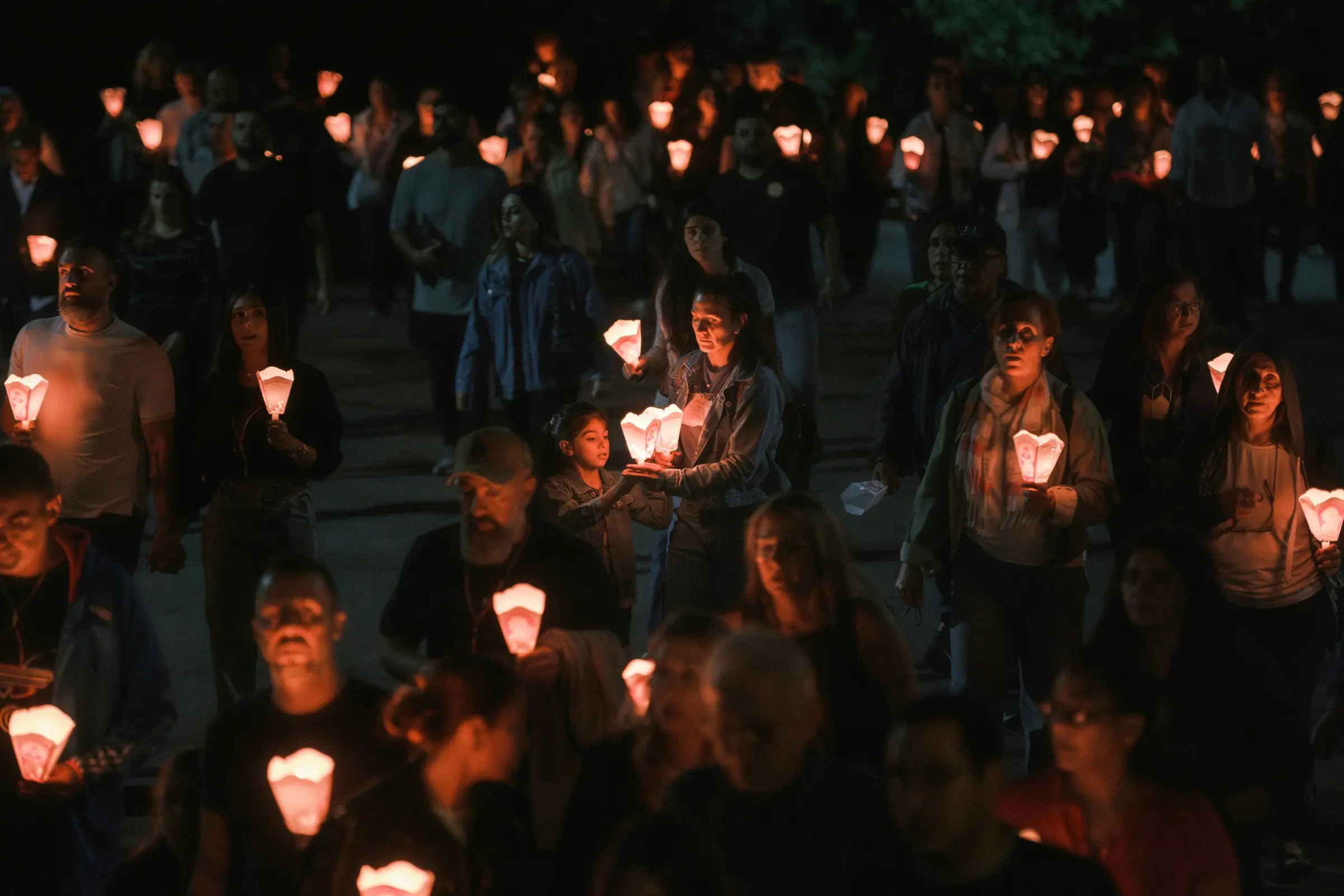 A crowd of people of all ages holding candles together at night
