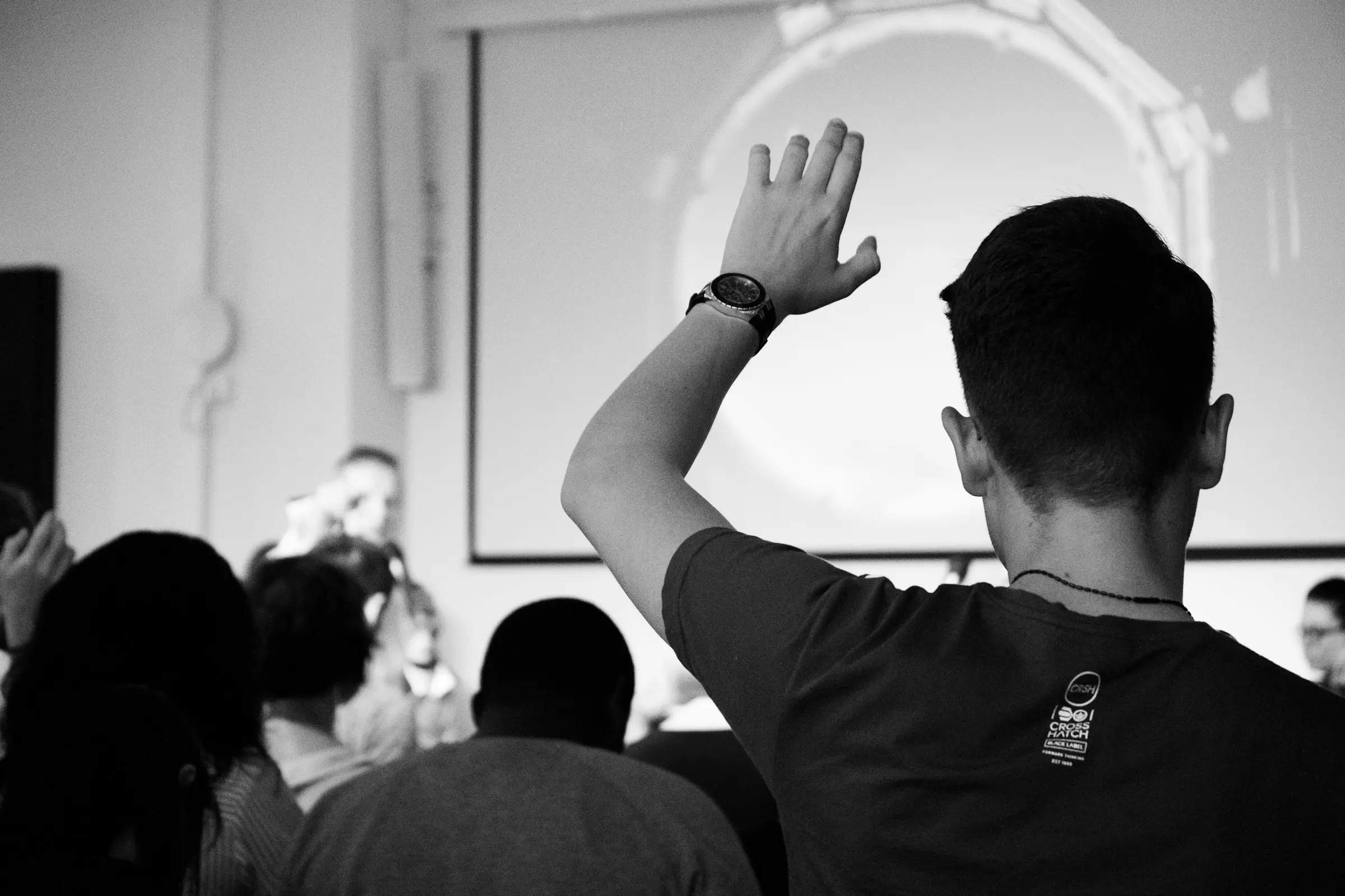A man in a packed room raising his hand to speak