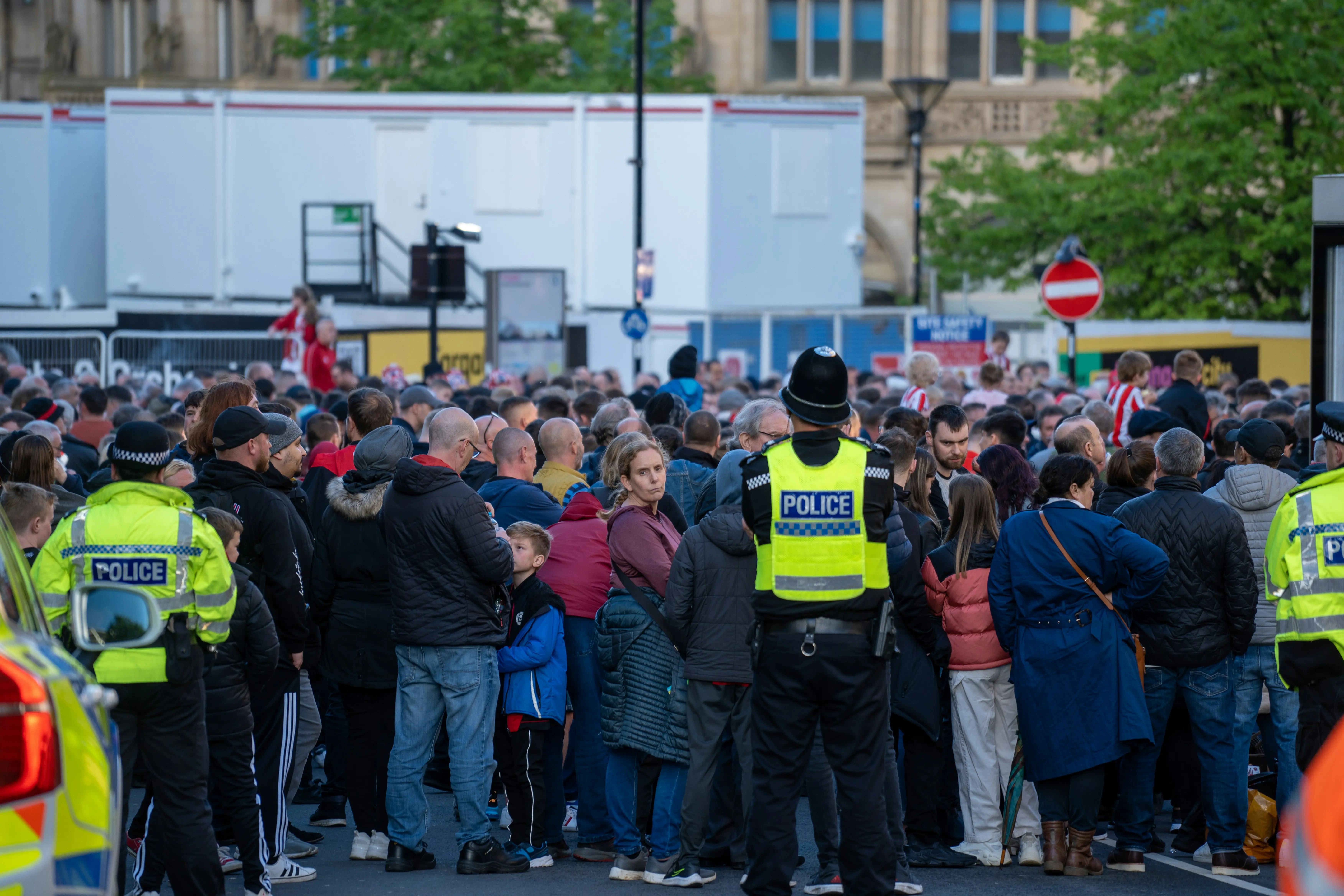 A packed crowd on a British street at dusk, police officers in hi-vis among them