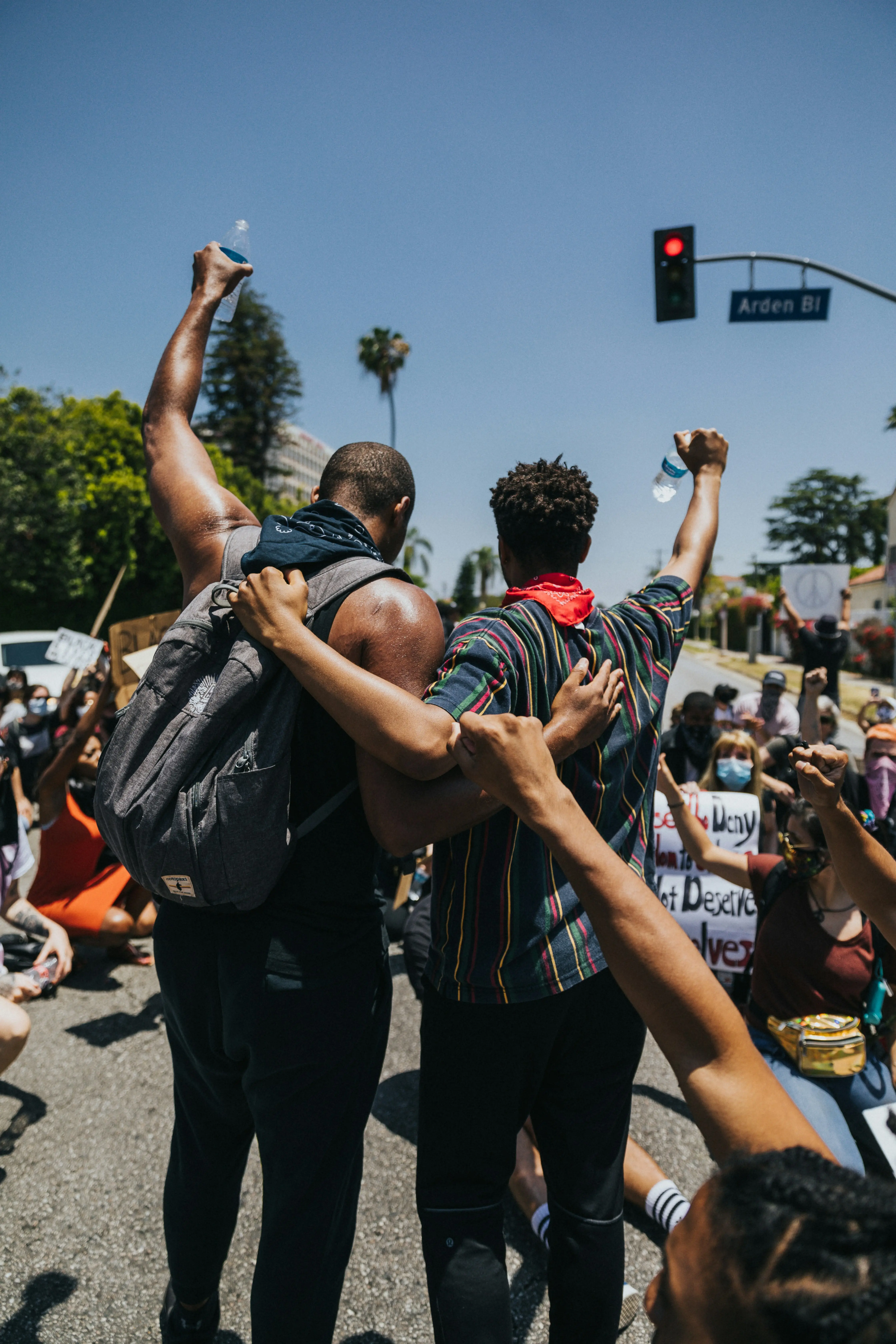 Two young men at a march, arms round each other, fists raised to a blue sky