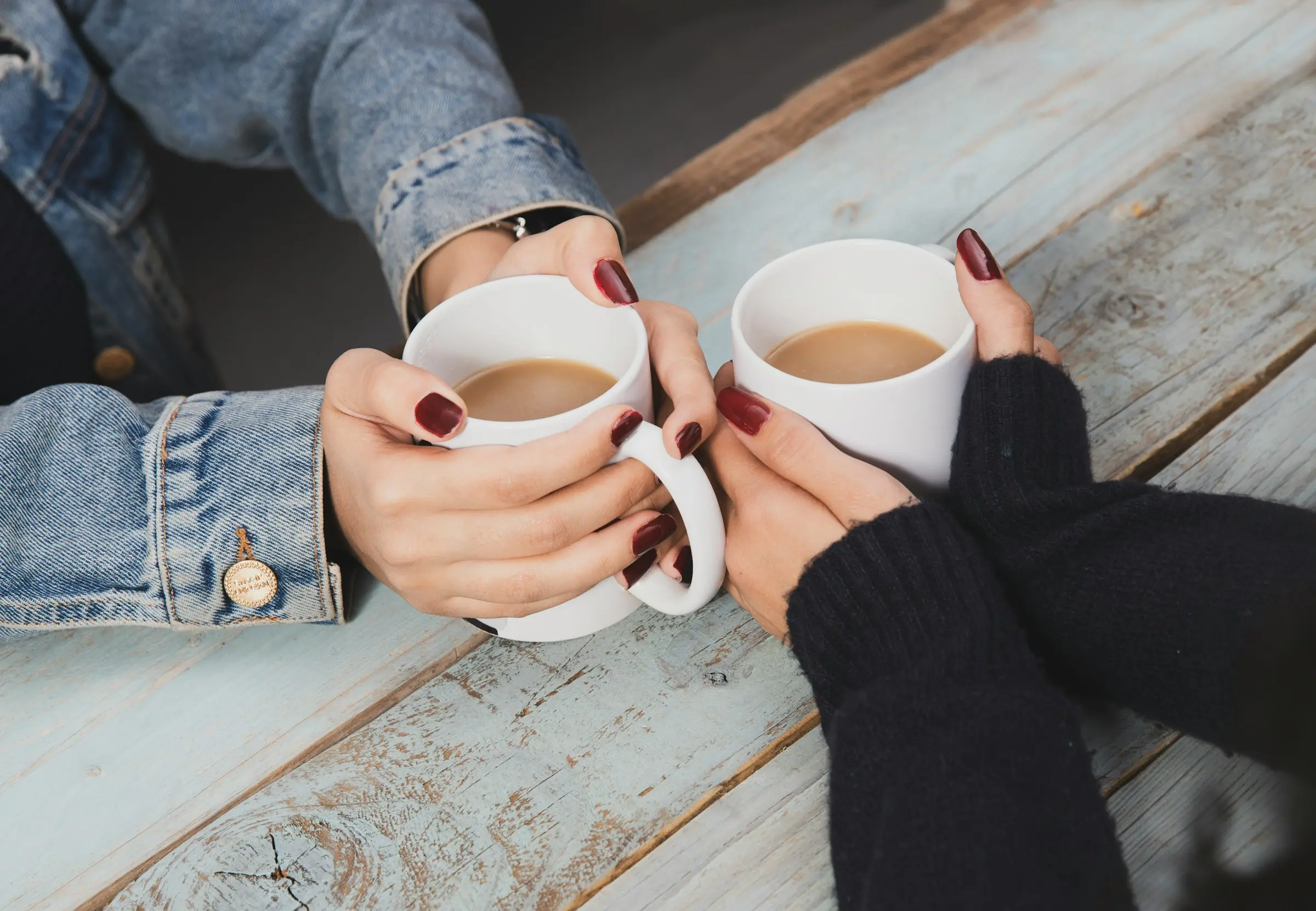 Two pairs of hands around mugs of milky tea on a wooden table
